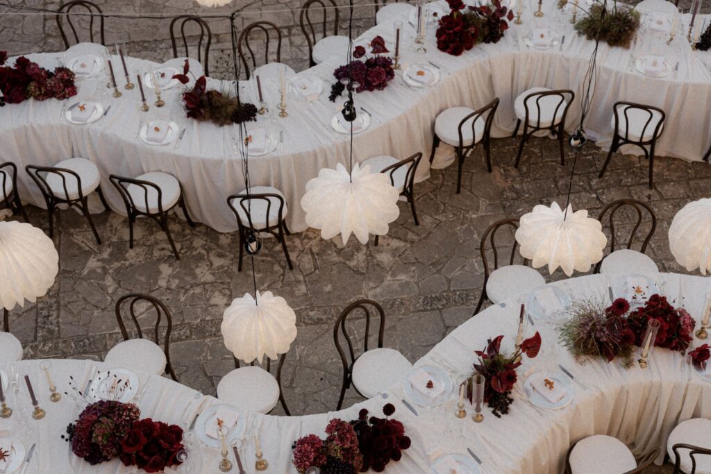 Serpentine tables at Villa Càrcara in Sicily with drapery, deep red and burgundy floral arrangements and lanterns. Shot by GAP photography.